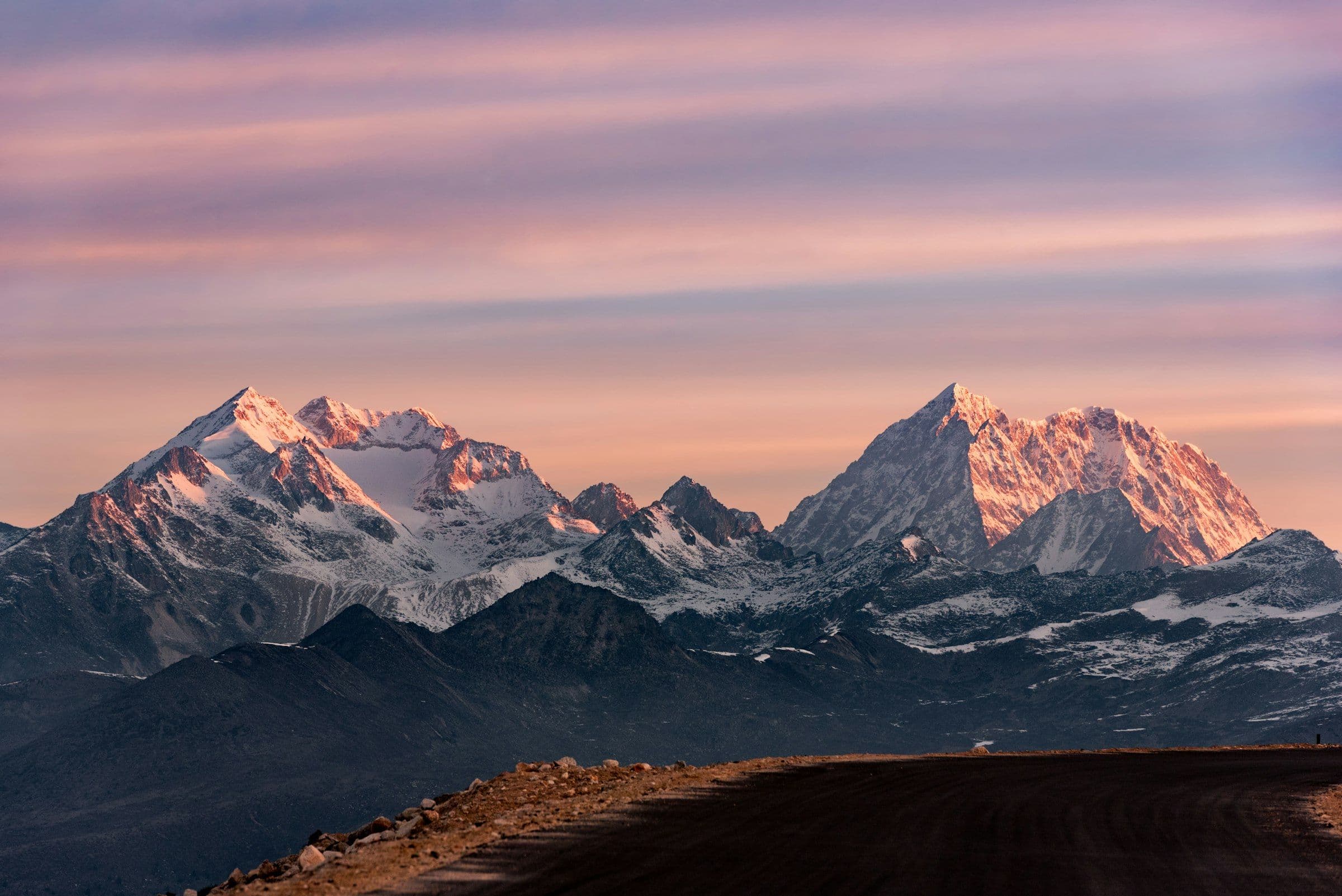 Pink alpenglow on twin snow peaks above a dark high plateau