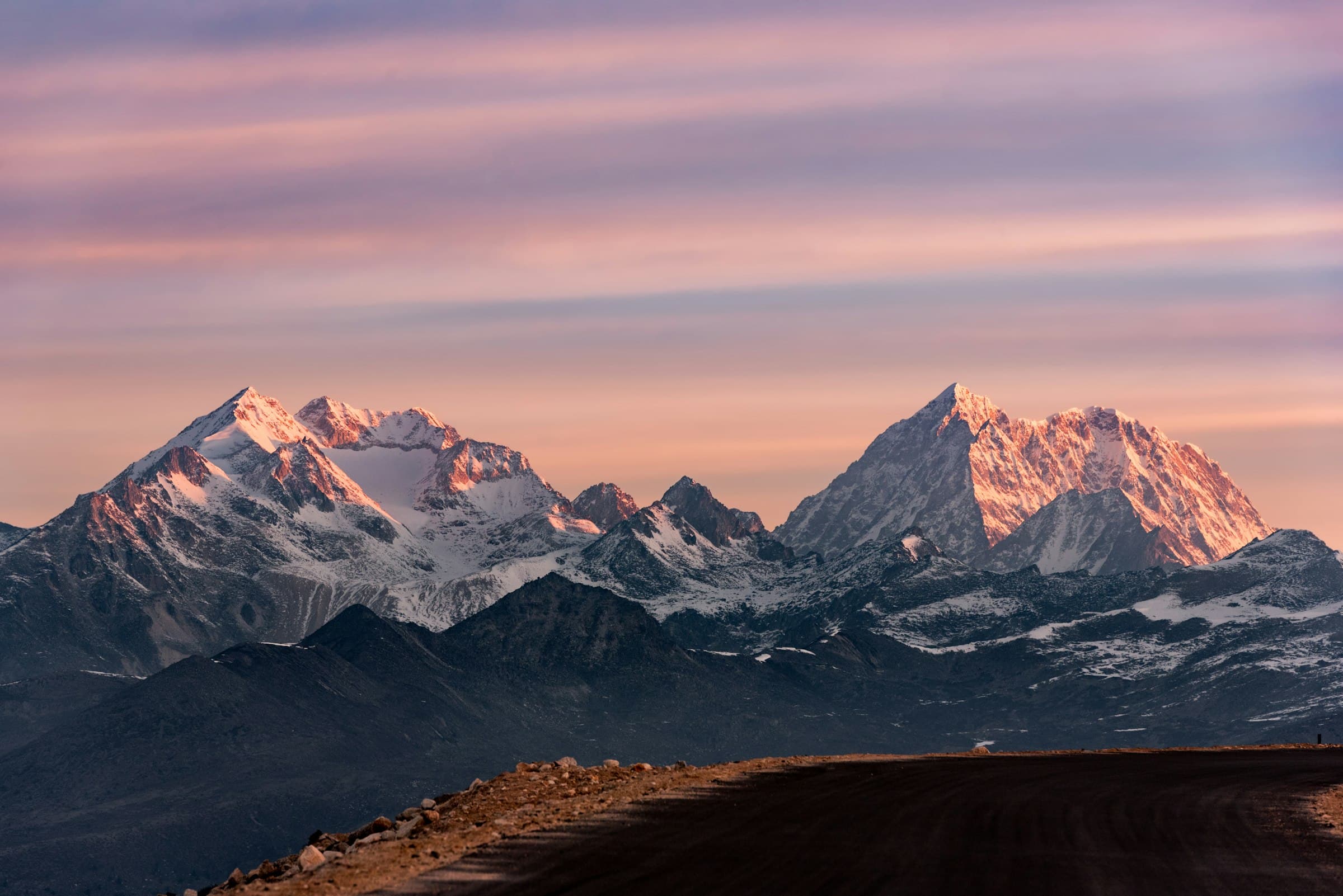 Pink alpenglow on twin snow peaks above a dark high plateau