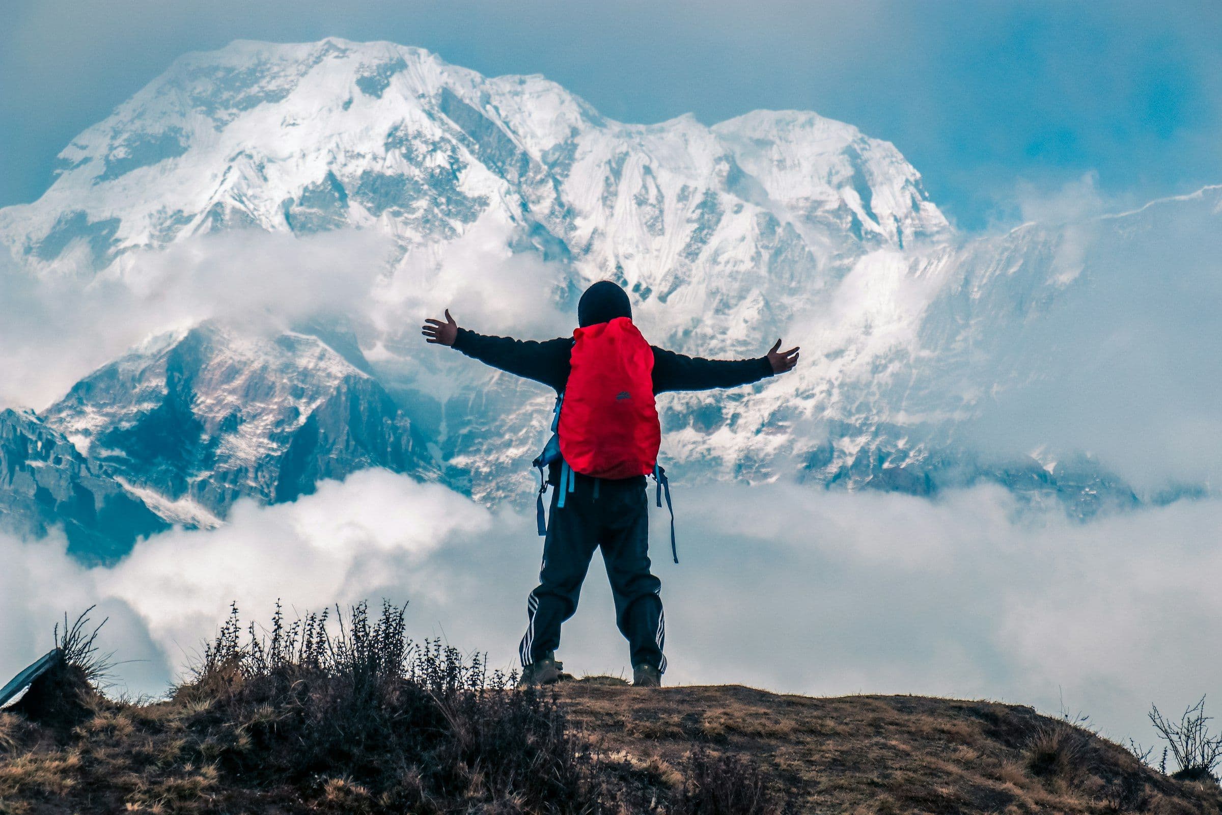Trekker with arms spread before a cloud-wrapped snow massif