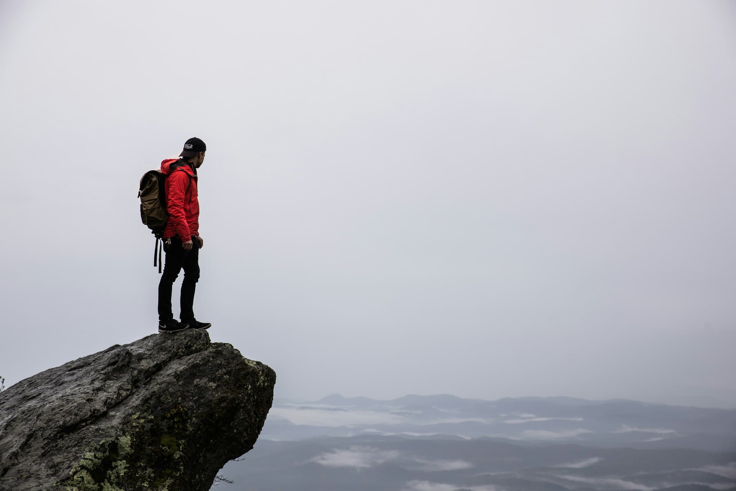 Trekker in a red jacket on a rocky overlook above a misted valley