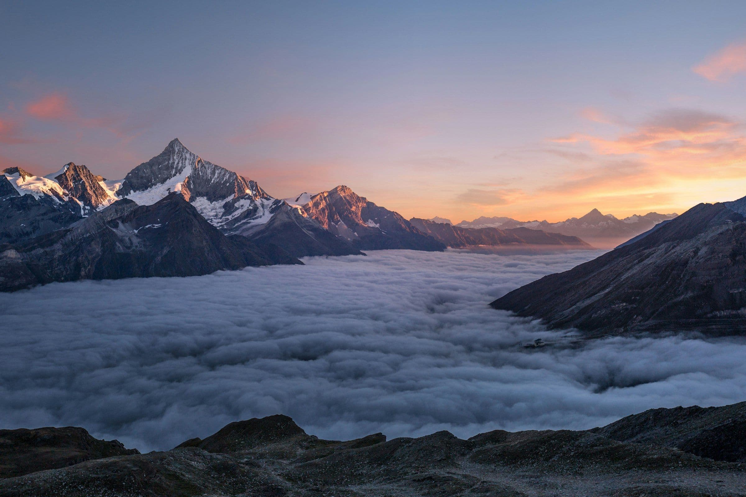 Snow peaks at sunrise above a sea of clouds filling the valleys